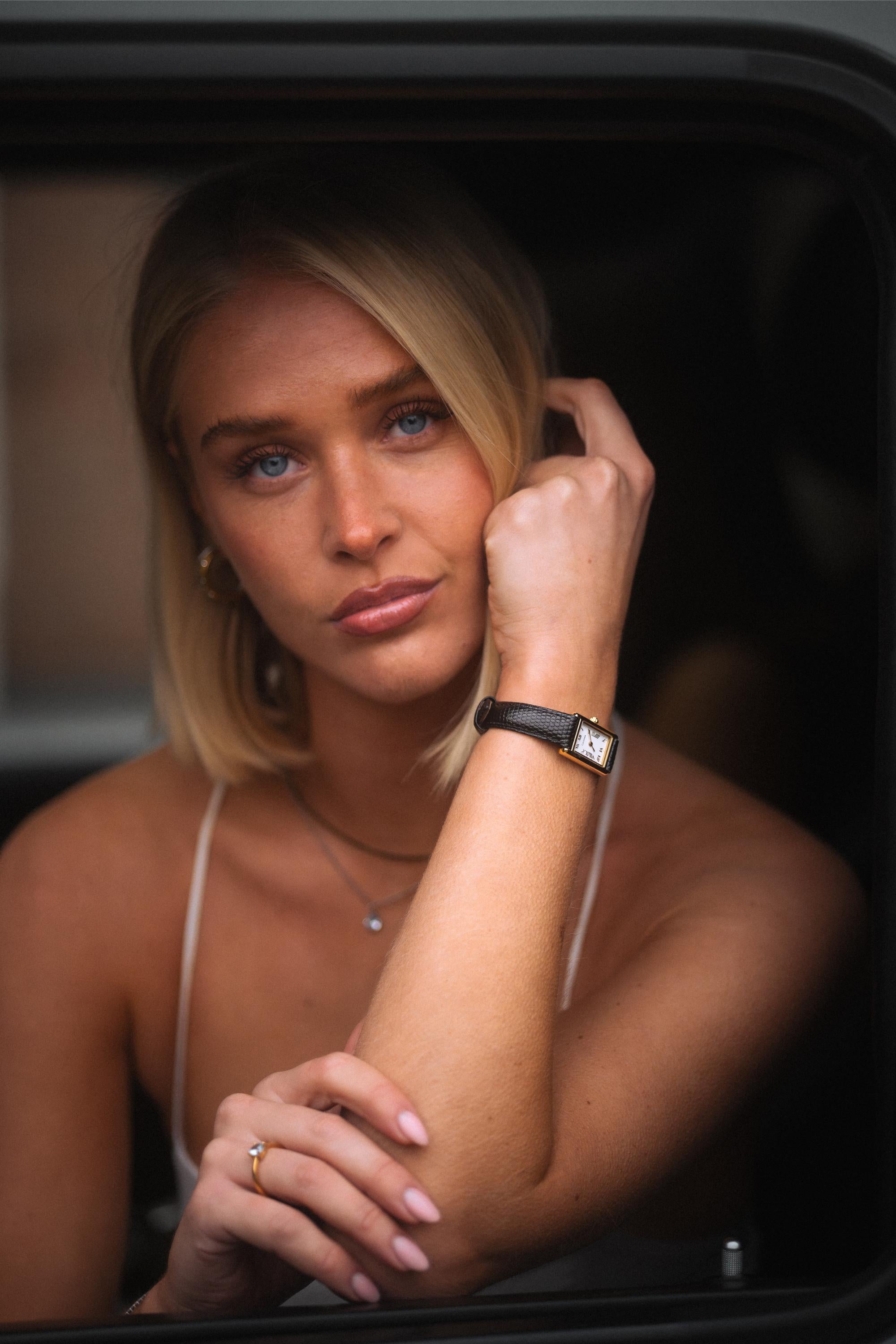 Lucienta Amara gold square women’s watch with black leather strap, elegantly styled on a model in a sophisticated outdoor setting.